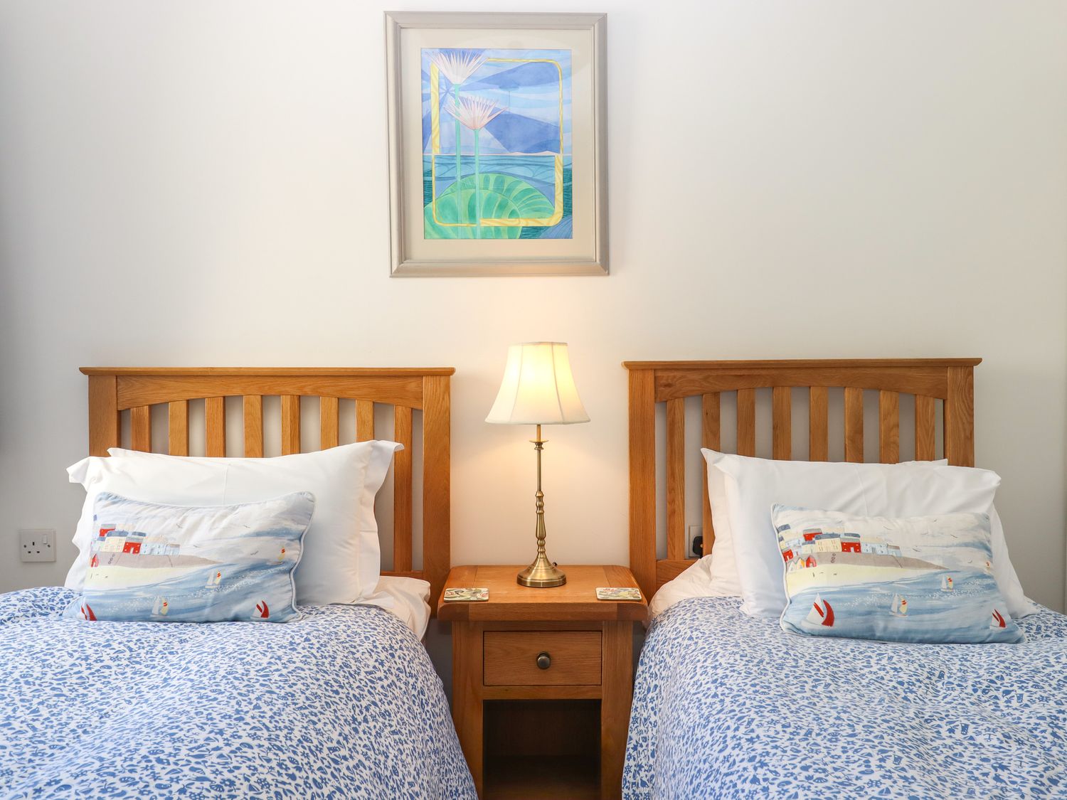 A bedroom with two single beds with wooden headboards a wooden nightstand with a lamp and a painting on the wall at 14 Burgh Island Causeway in Bigbury-On-Sea