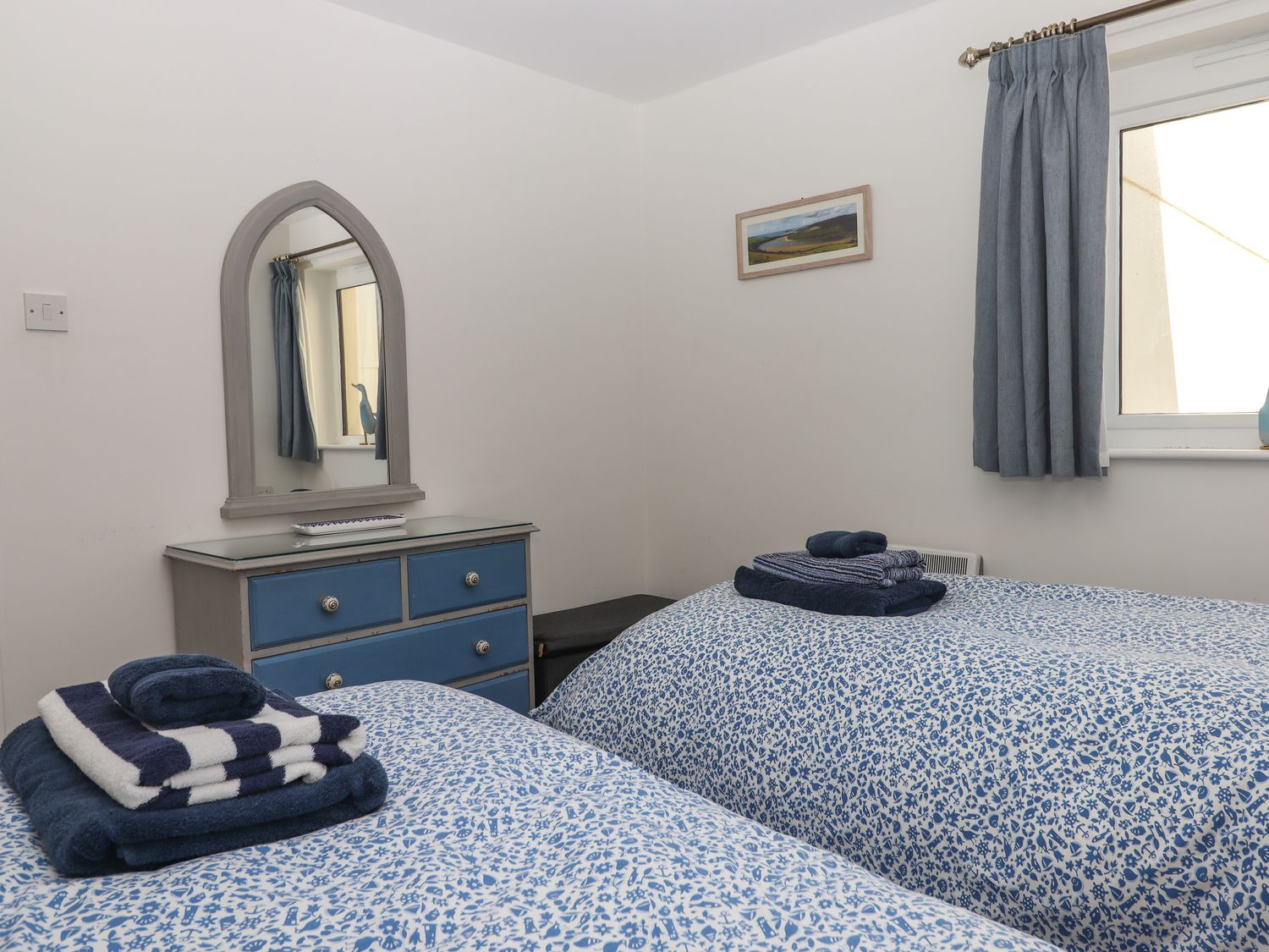A bedroom with two single beds blue patterned bedspreads blue dresser with mirror and blue curtains at 14 Burgh Island Causeway Bigbury-On-Sea