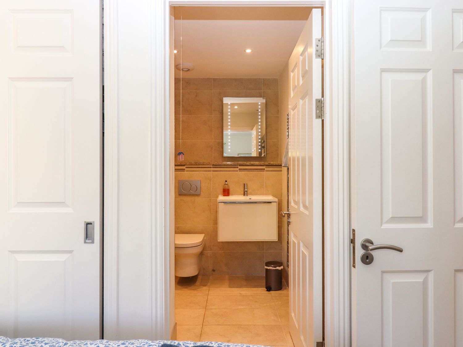 A bathroom with a wall-mounted toilet and sink a mirror and a small trash bin at 14 Burgh Island Causeway Bigbury-On-Sea