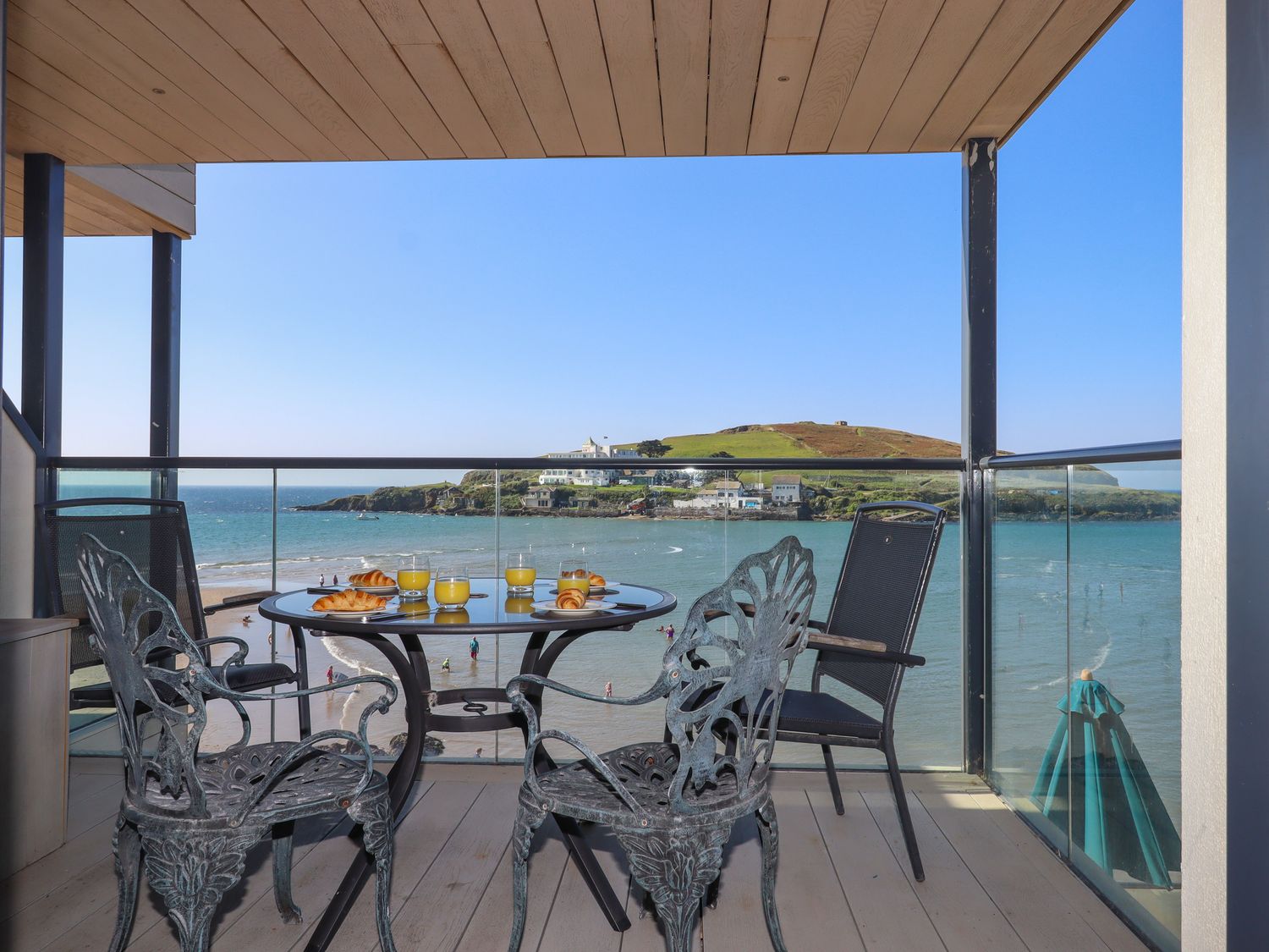 A balcony with a table set with croissants and glasses of orange juice overlooking a beach and an island at 14 Burgh Island Causeway in Bigbury-On-Sea