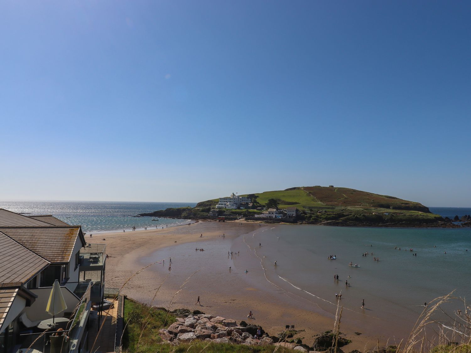 A beach with people swimming and walking near an island with buildings at 14 Burgh Island Causeway in Bigbury-On-Sea