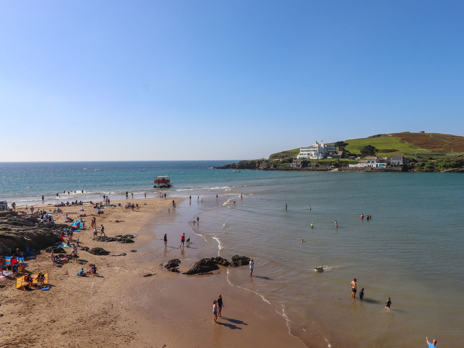 A beach with people on sand and in water near a coastal hill with buildings at 14 Burgh Island Causeway in Bigbury-On-Sea