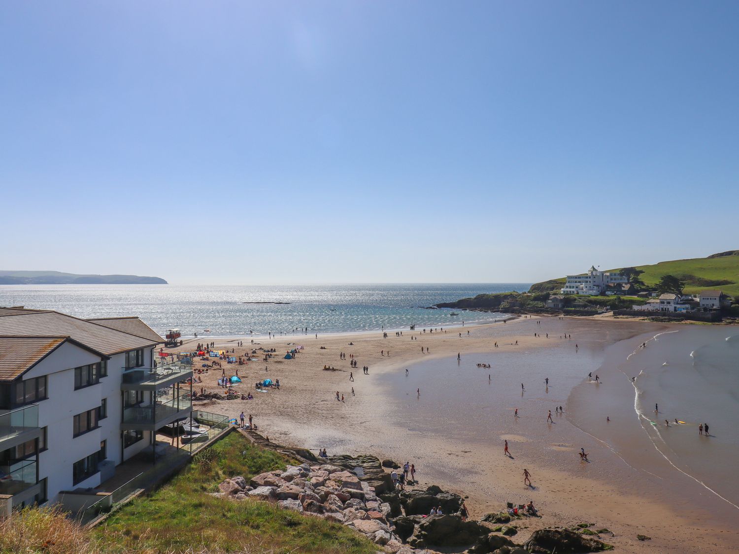 A sandy beach with people near residential buildings and green hills at 14 Burgh Island Causeway in Bigbury-On-Sea