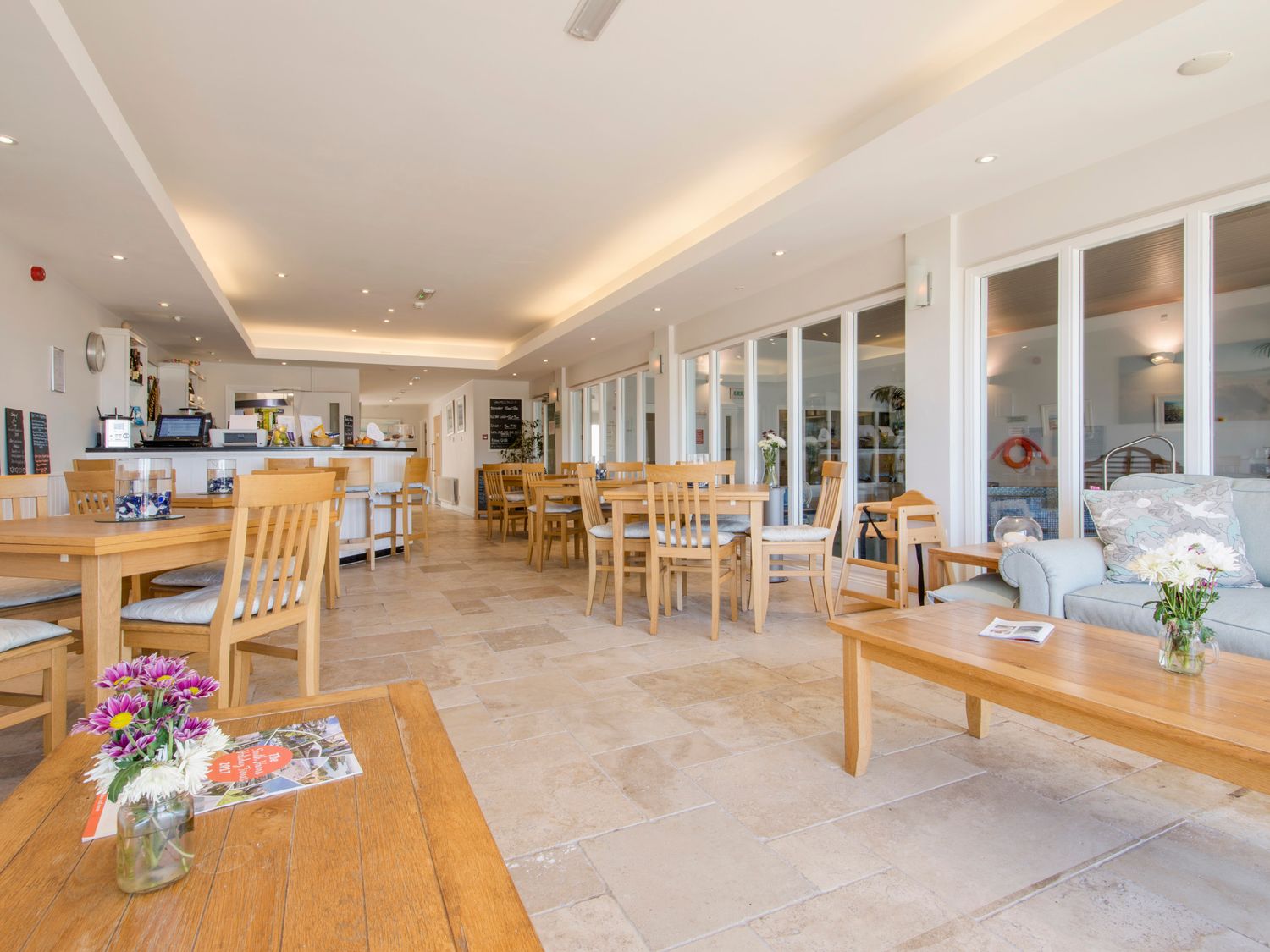 A dining area with wooden tables and chairs and a seating area with a sofa and flowers on the table at 14 Burgh Island Causeway in Bigbury-On-Sea