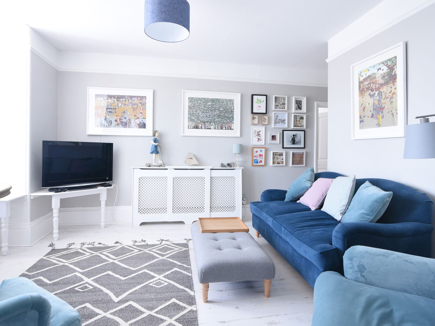 A living room with blue sofas grey ottoman and a television at Coastal View in Lyme Regis