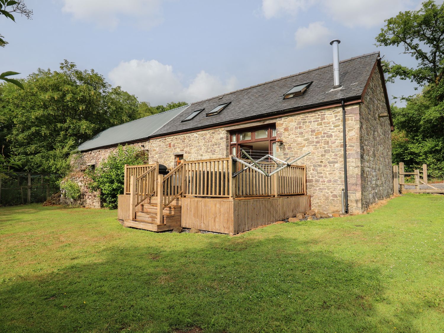 A stone barn with a wooden deck and grassy yard at Gelli Barn Near Llandeilo