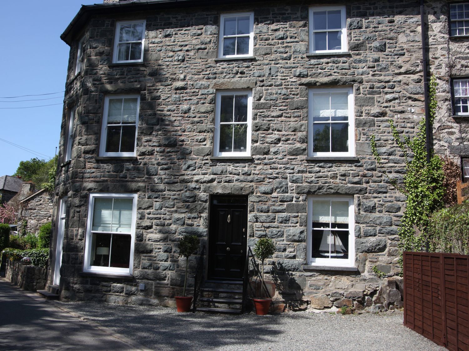 A stone house with white window frames and a black door with potted plants outside at Gwynfryn House in Llanbedr
