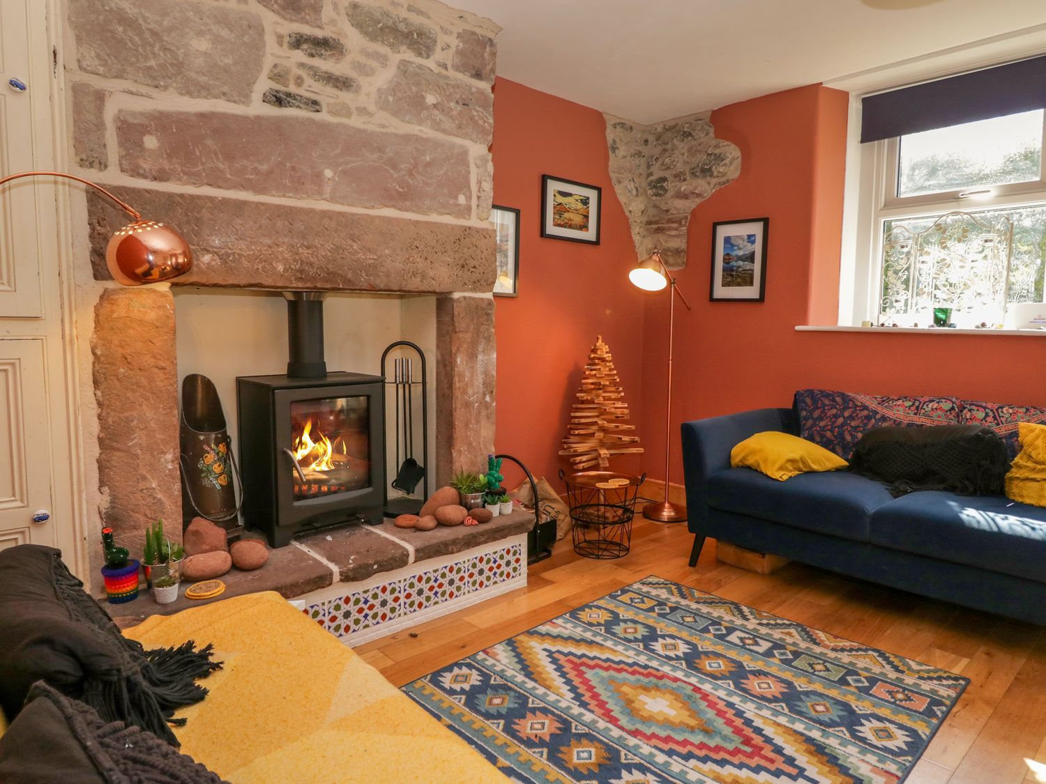 A living room with a lit fireplace blue and yellow sofas and a patterned rug at Whitecroft Nook in Gosforth