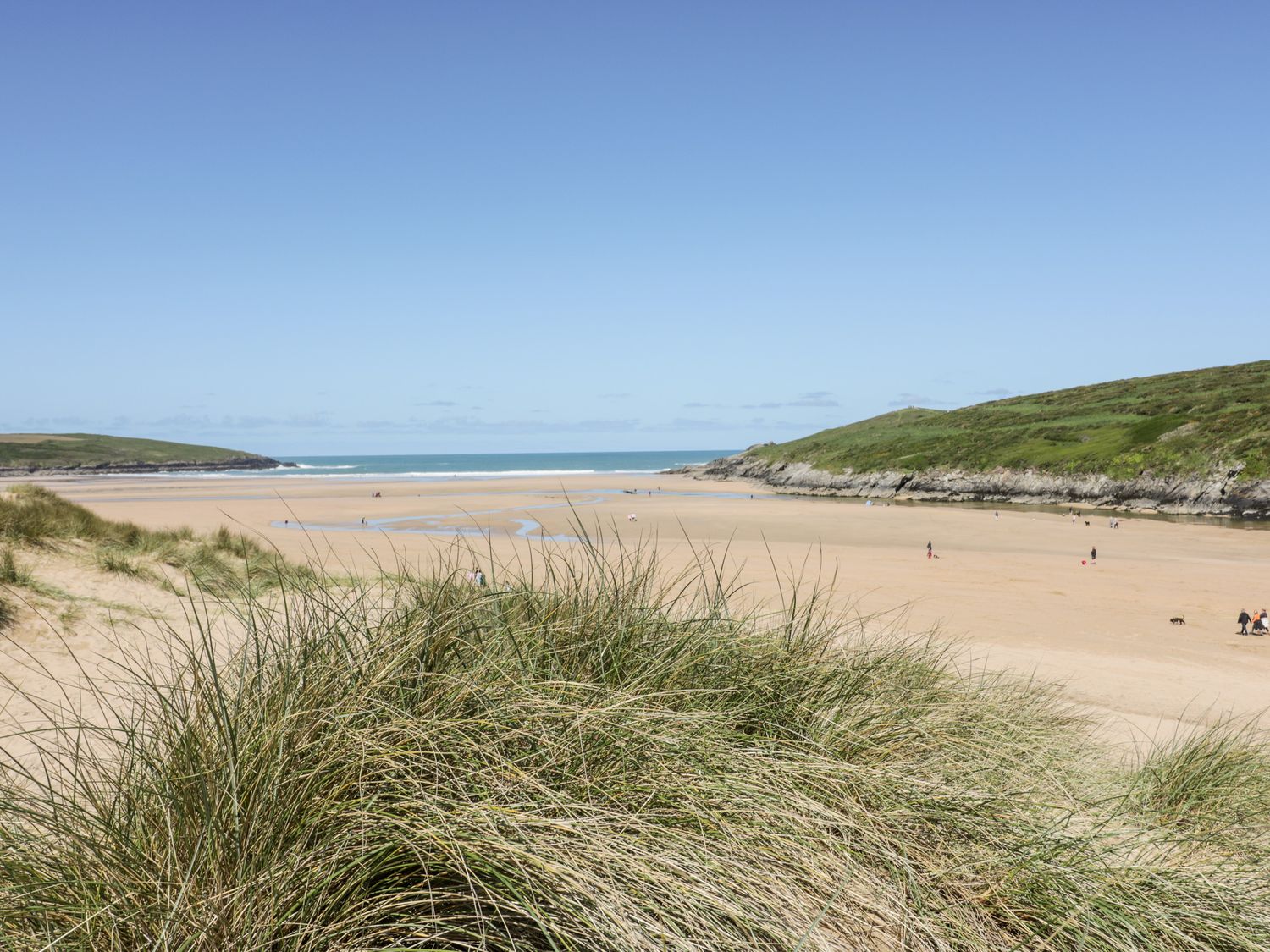 A sandy beach with grassy dunes and hills in the background at Far Horizons in Newquay