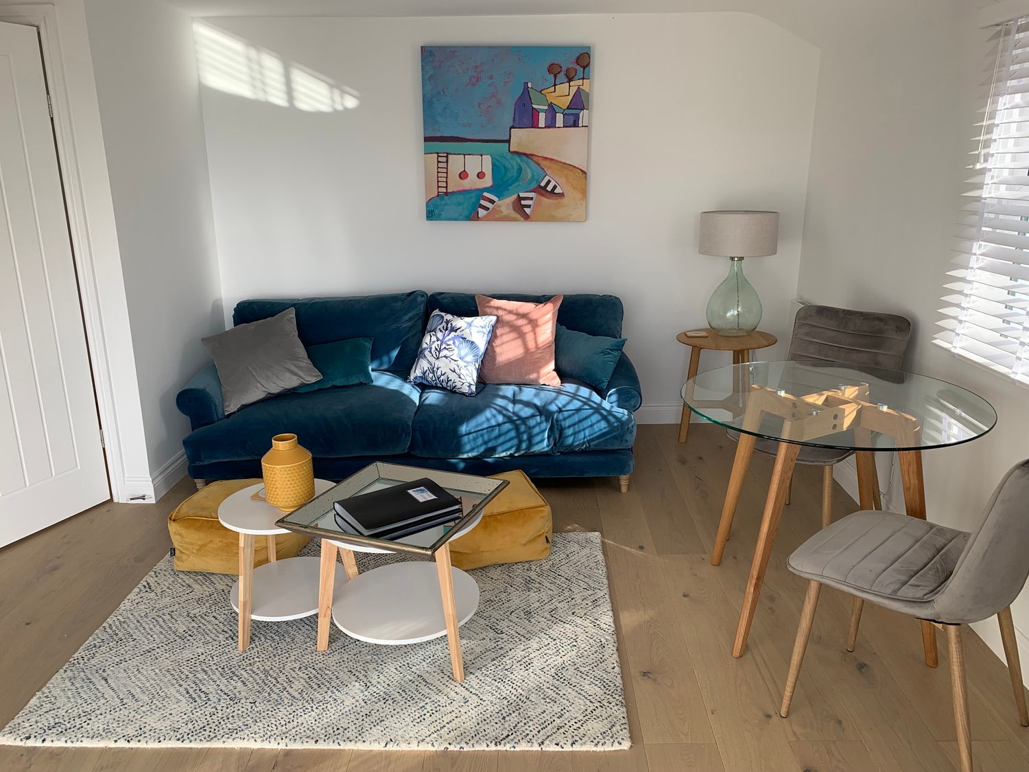 A living room with a blue sofa cushions coffee tables and a glass dining table with chairs at Beach Cottage in Cadgwith