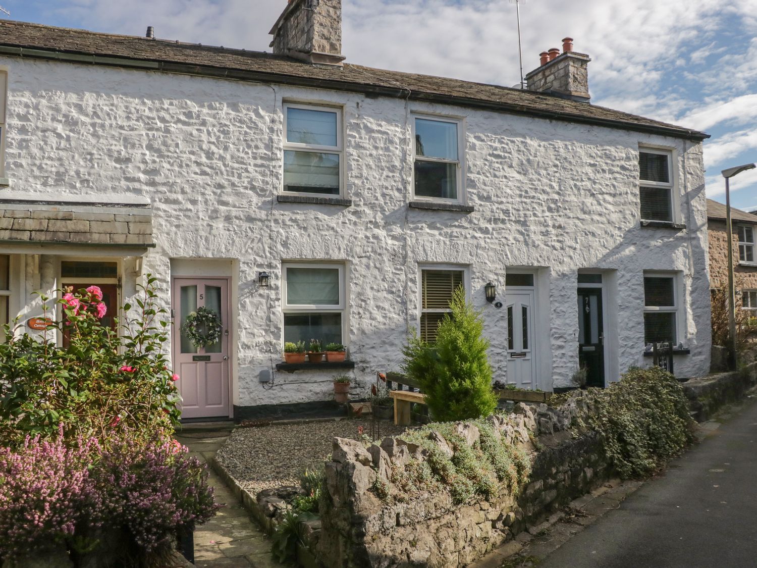 A row of white stone cottages with numbered doors and small front gardens along a street at Gosling Cottage in Kendal
