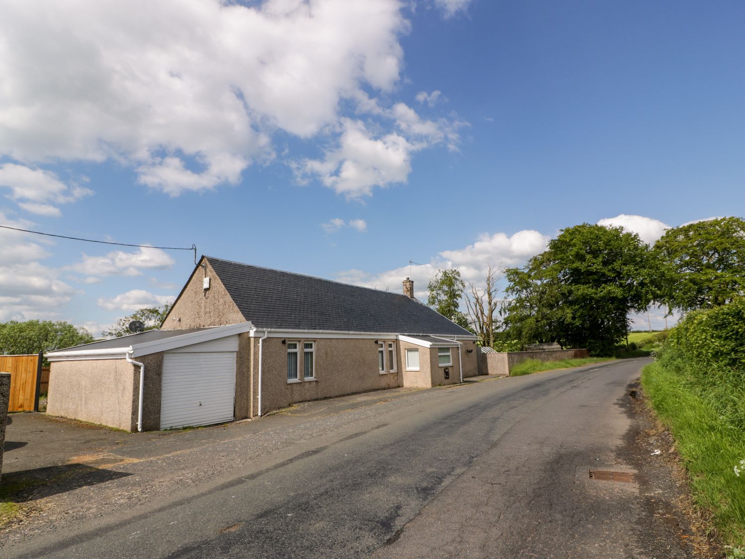 A bungalow with a garage along a rural road with trees and grass in the background at Largieholm in Mauchline
