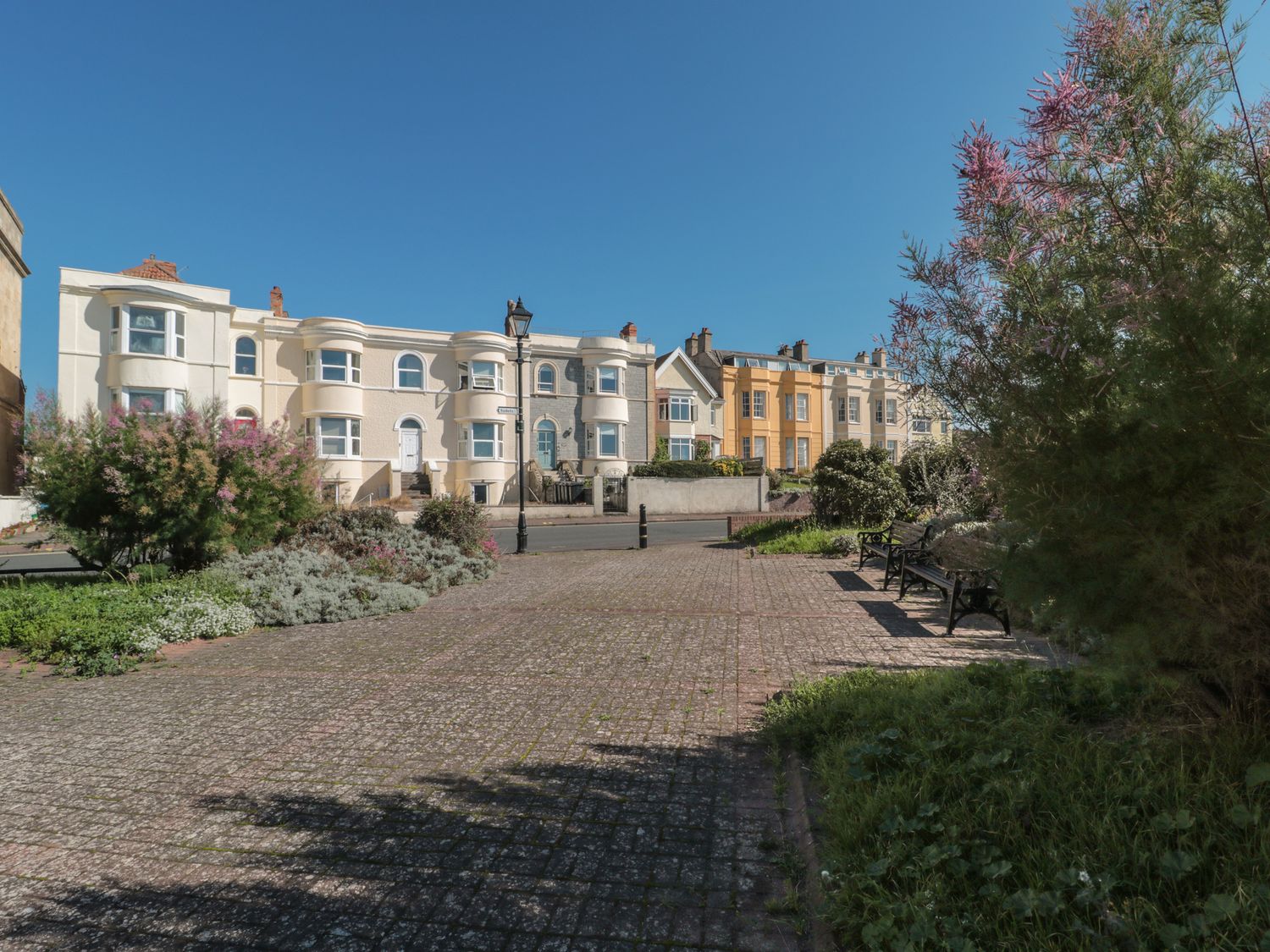 Outdoor paved area with benches shrubs and flowering plants in front of residential buildings at 49 Esplanade in Burnham-On-Sea