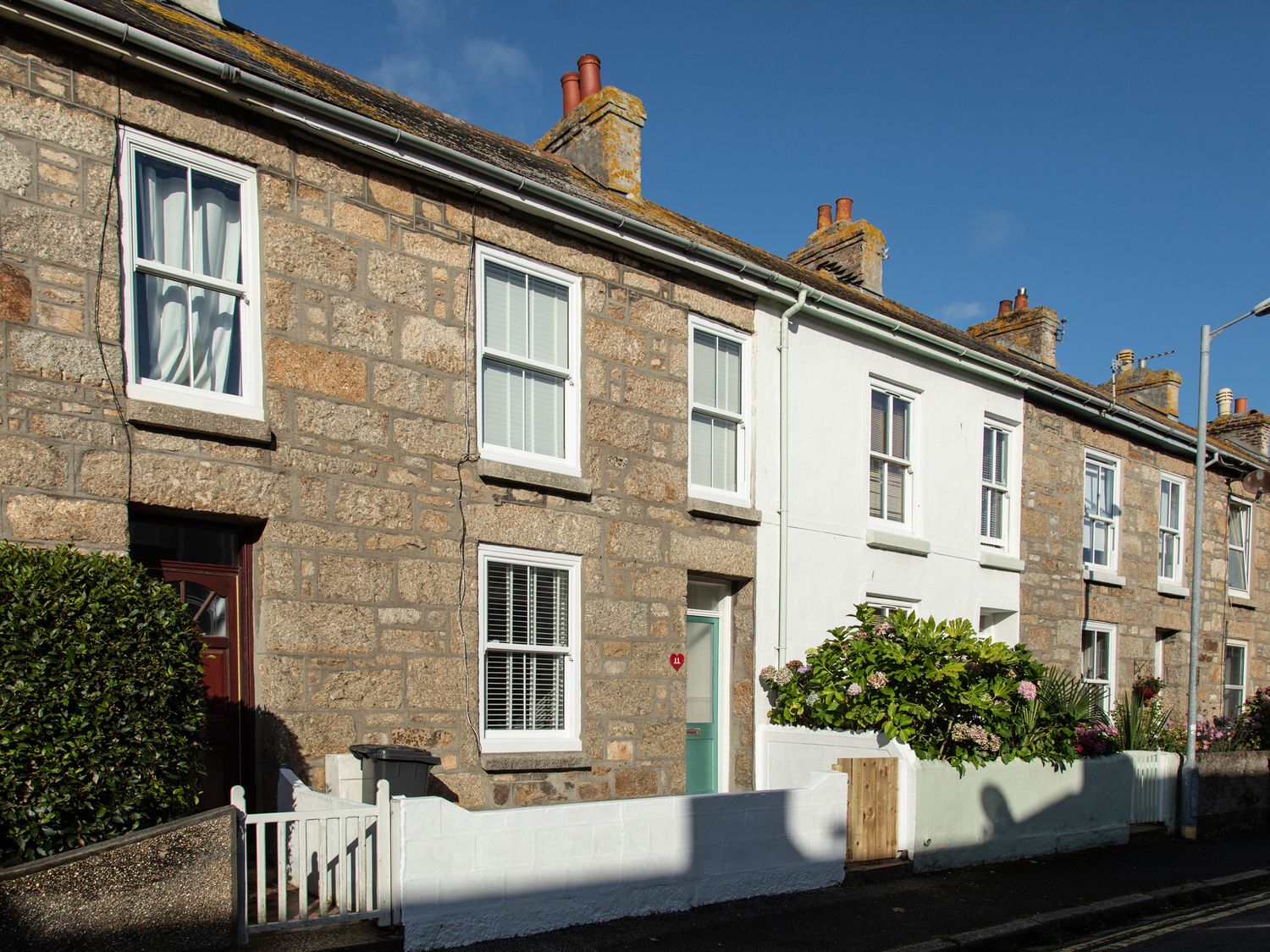A row of stone and white terraced houses with small front gardens on a street at 11 Belgravia Street in Penzance