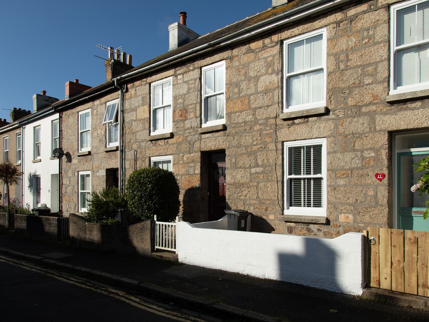 A row of stone and brick terraced houses with white windows and front gardens at 11 Belgravia Street in Penzance