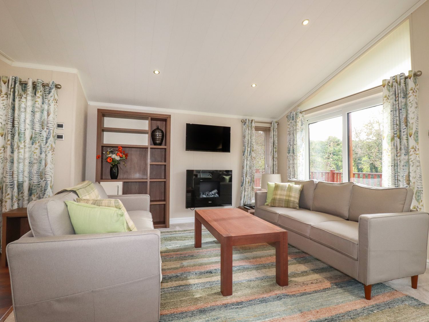 A living room with two sofas a wooden coffee table and a wall-mounted TV at Haven Lodge in Bossiney Bay near Tintagel