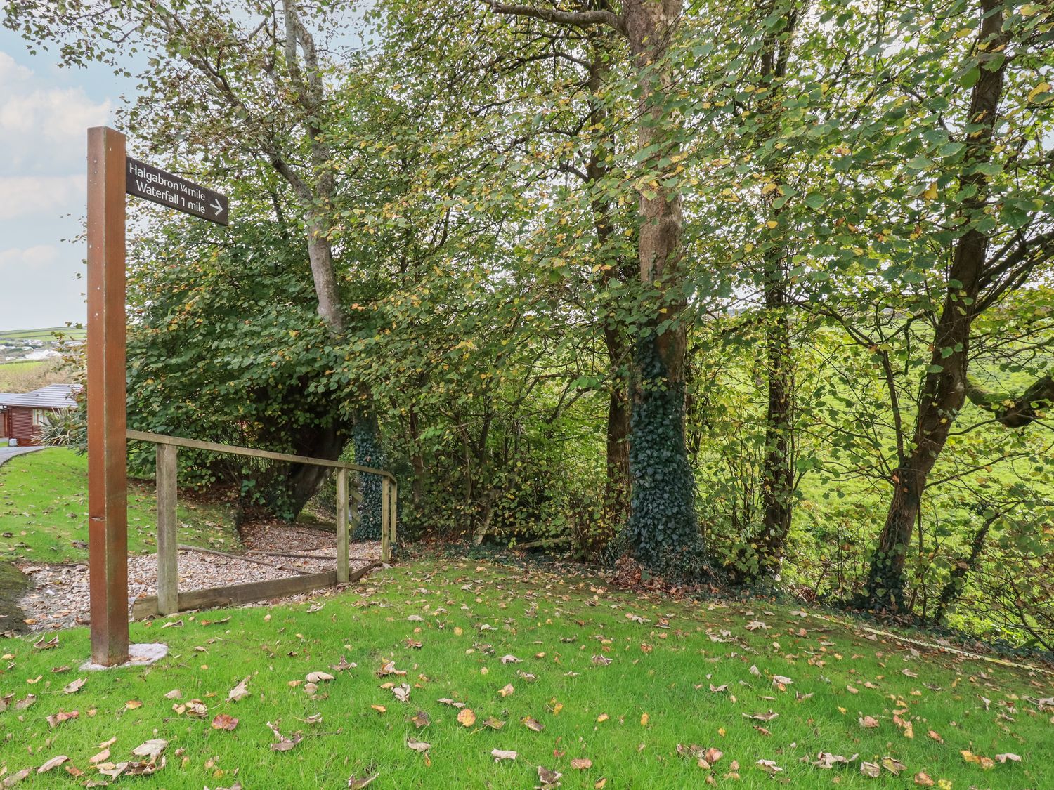 A grassy area with trees and a wooden signpost showing direction to Halgabron and Waterfall at Haven Lodge in Bossiney Bay near Tintagel