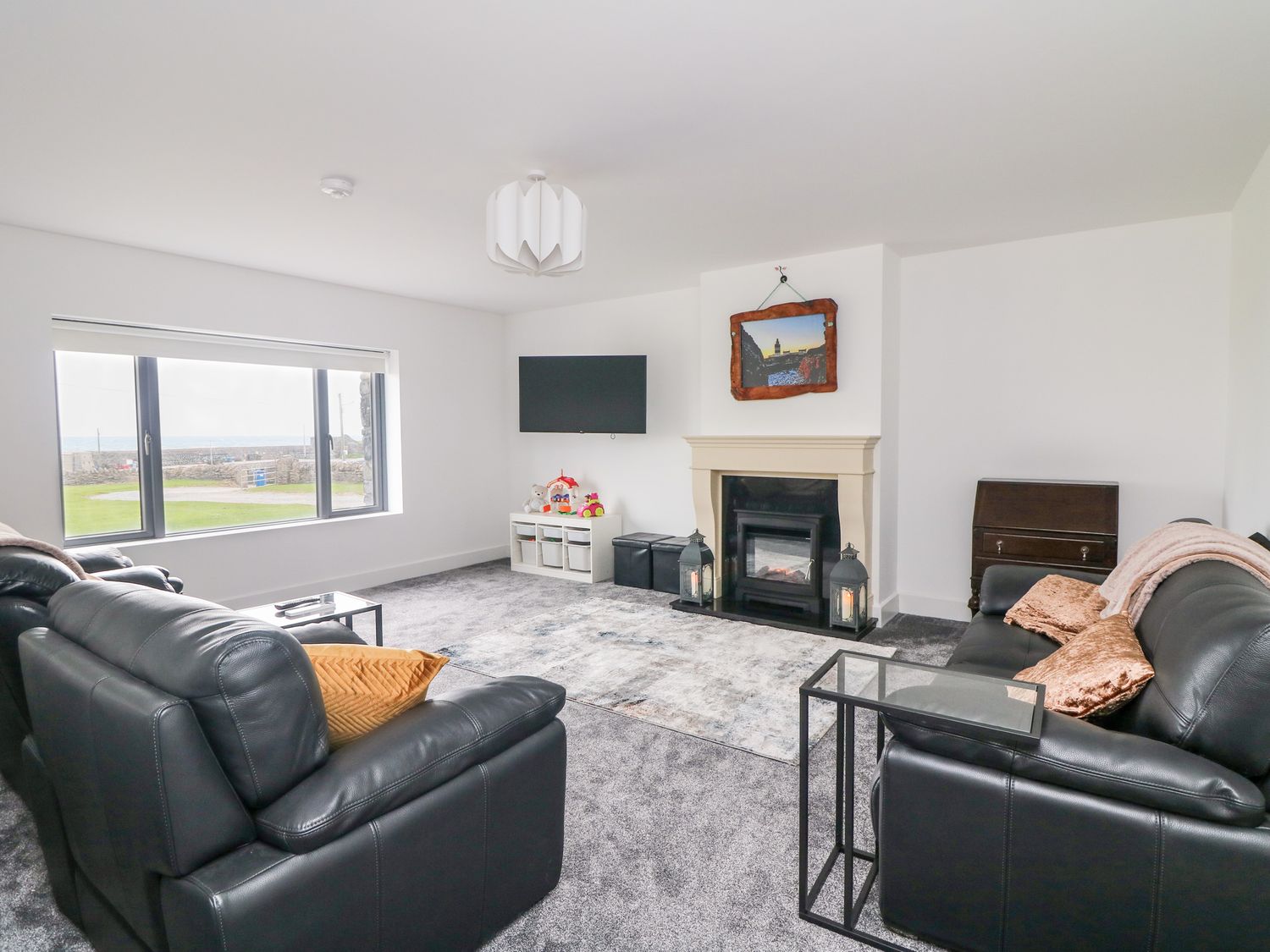 A living room with black leather sofas a fireplace and a wall-mounted television at Old Field House Slade near Fethard-On-Sea County Wexford