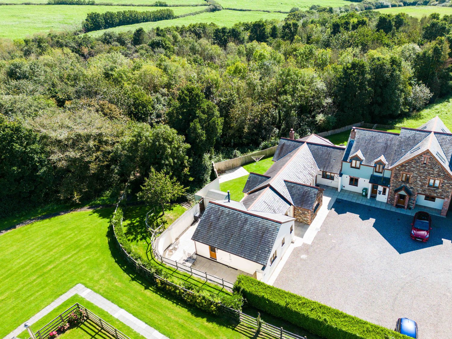 An aerial view of a large house with a driveway and green lawn surrounded by trees at Chy Pol in St Minver