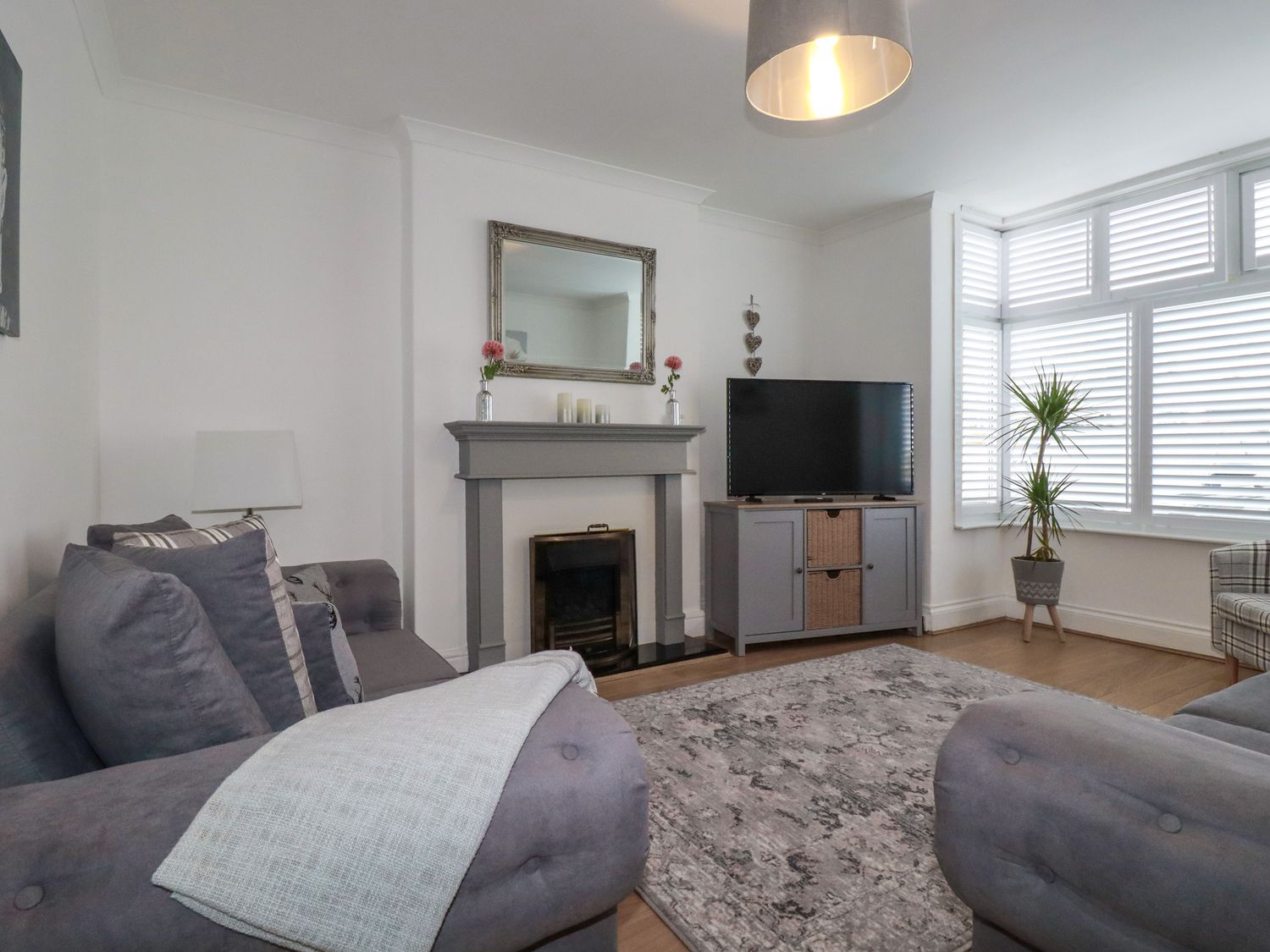 A living room with two gray sofas a gray fireplace a television on a cabinet a plant by the window and a patterned rug at 119 Henver Road in St Columb Minor