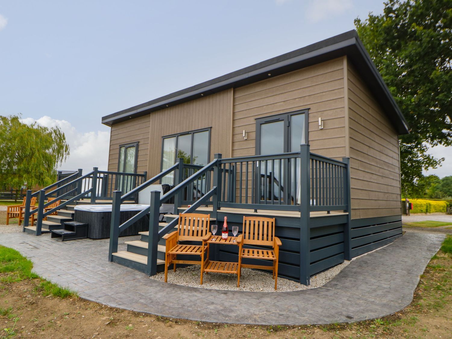 Exterior of a modern cabin with a raised porch and wooden chairs with a bottle and glasses on a table at Bowes Hideaway in Eppleby