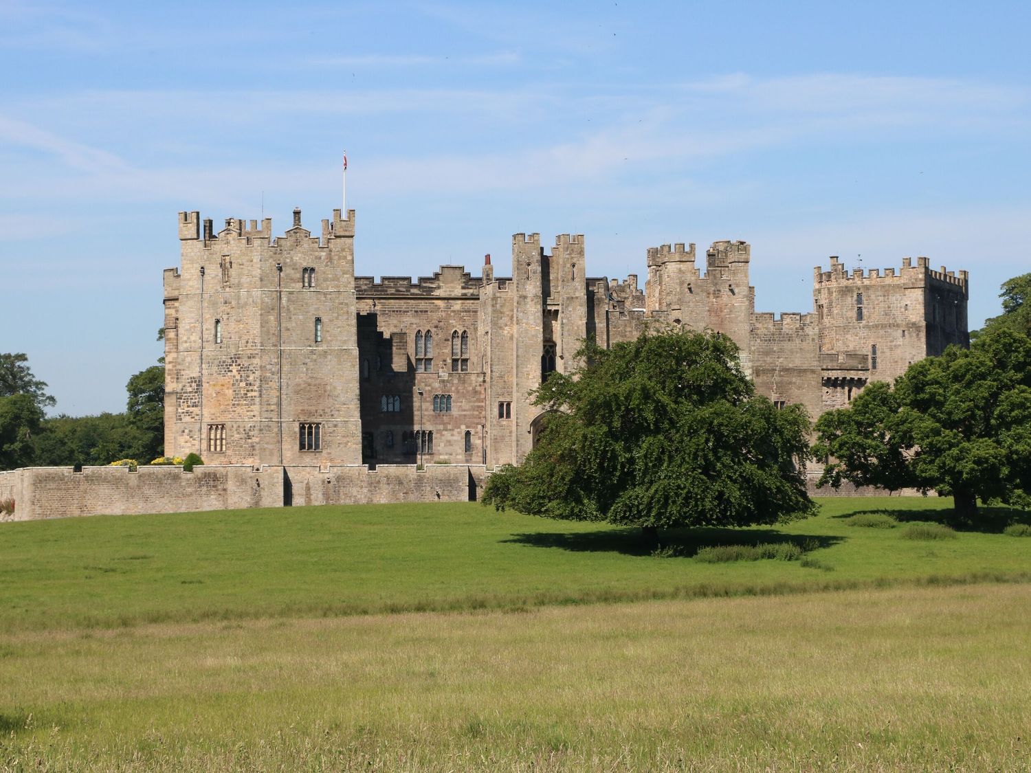 A stone castle with battlements surrounded by a green field with trees at Bowes Hideaway in Eppleby