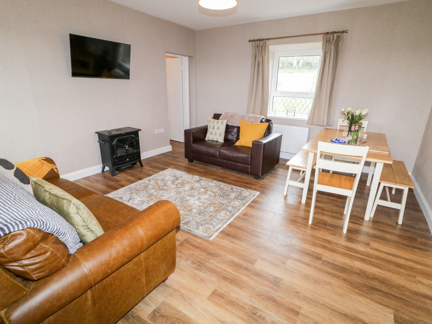A living room with two sofas a wall mounted TV a small stove and a dining table with chairs at Rose Cottage in Omagh