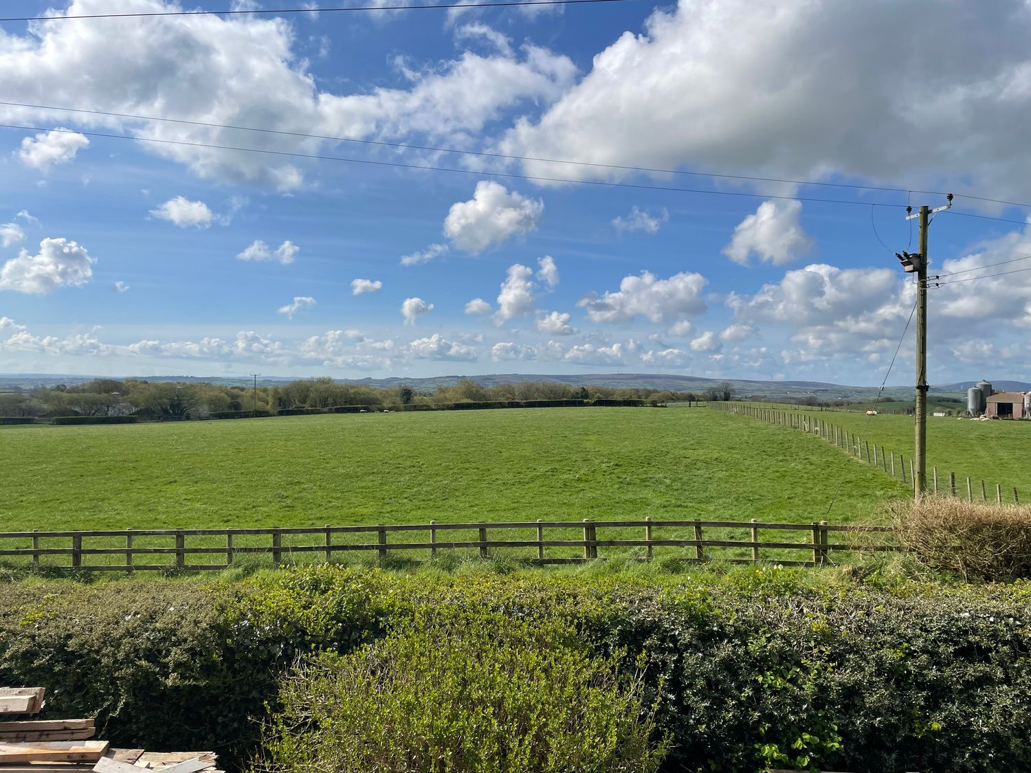 A green field with a wooden fence and power lines under a partly cloudy sky at Rose Cottage in Omagh