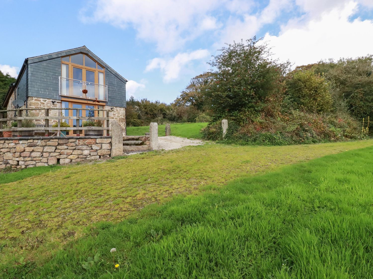 A stone and wood house with a balcony and garden surrounded by grass and trees at The Orchard in Cardinham