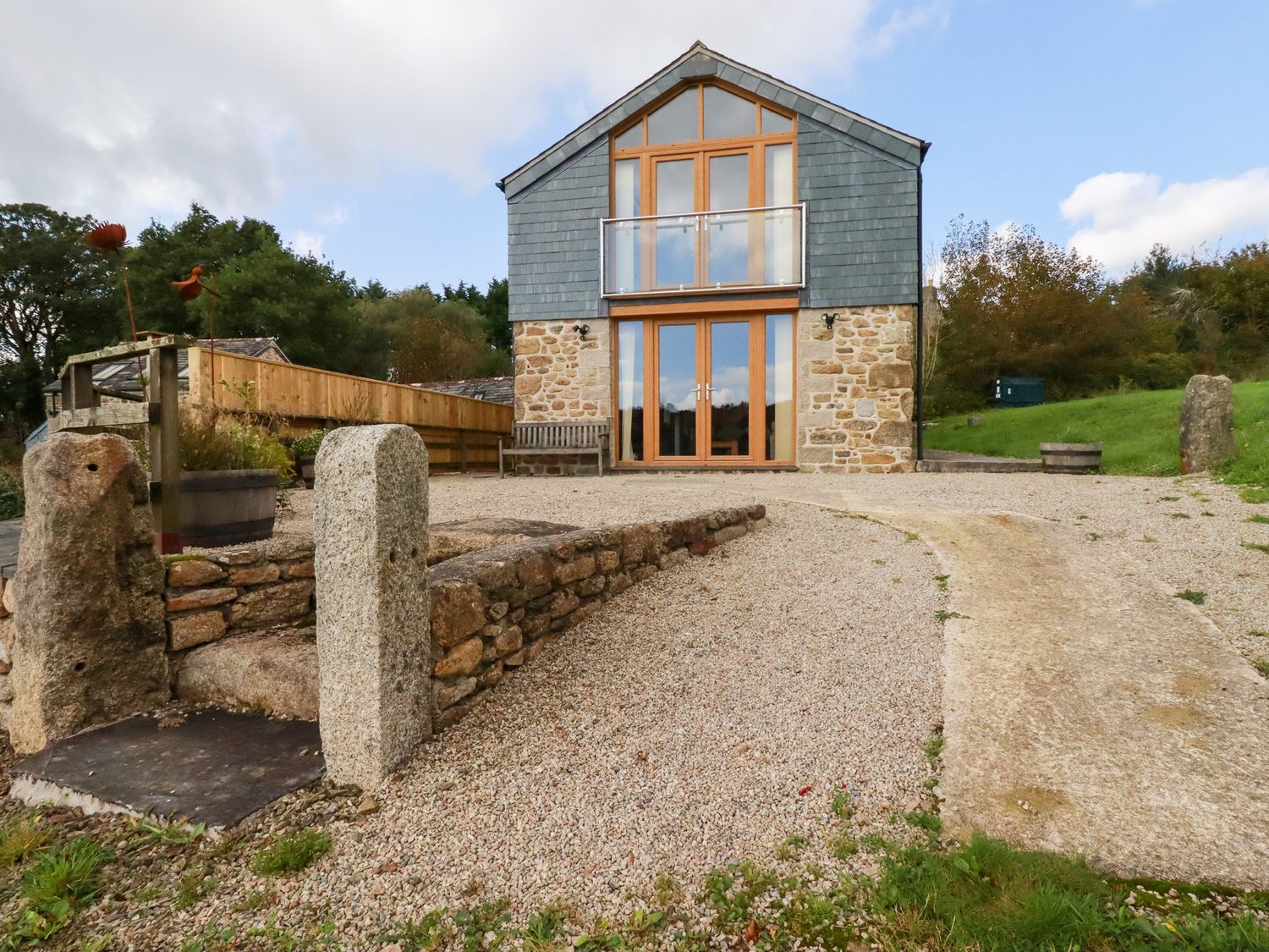 A two-story stone and wood house with glass balcony and gravel driveway at The Orchard in Cardinham