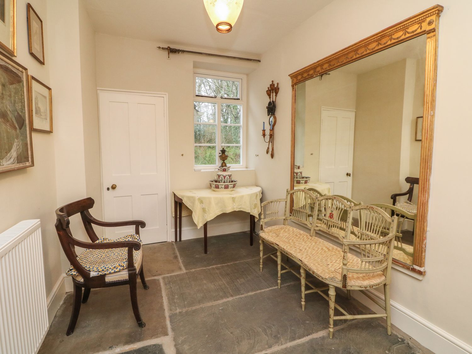 A small room with two chairs a table with a cloth and decorative items a large wall mirror and framed pictures on the wall at Laundry Cottage in Clovelly