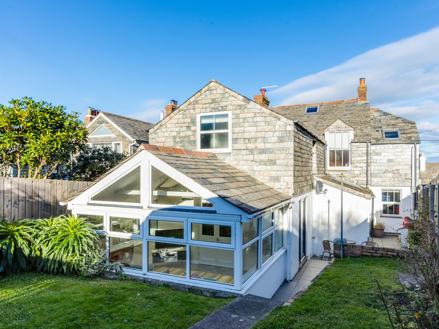 A stone house with a white conservatory and garden in the foreground at Tre Lowen in Port Isaac
