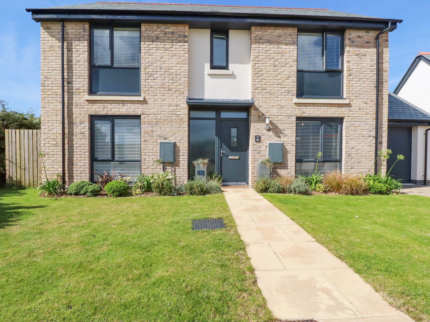 A front view of a two-story house with a paved walkway and garden at Cobalt in St Eval near Mawgan Porth