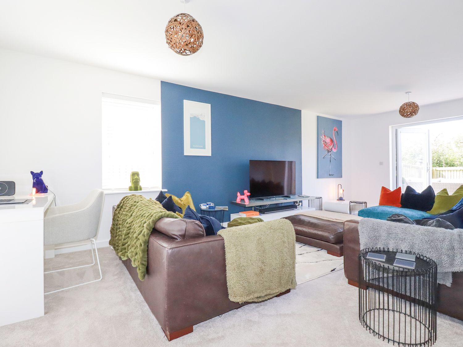 A living room with blue accent wall a television brown leather sofas and colorful cushions at Cobalt in St Eval near Mawgan Porth