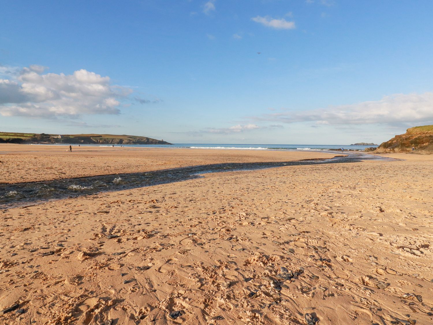 A beach with footprints on the sand a stream flowing to the sea and cliffs in the distance at Cobalt St Eval near Mawgan Porth