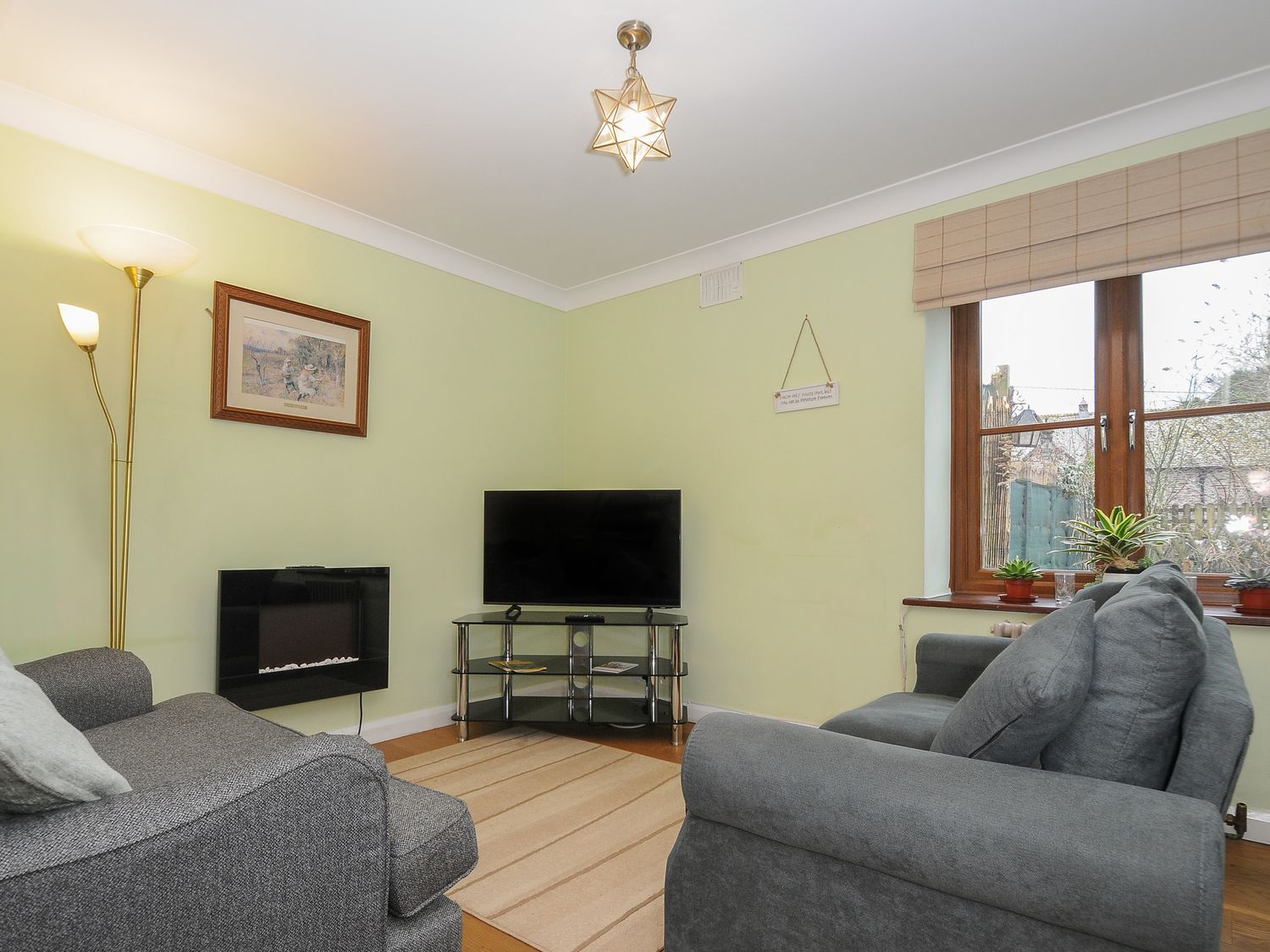 A living room with grey sofas a television on a glass stand a floor lamp and a window with plants at Rainbows End Launceston