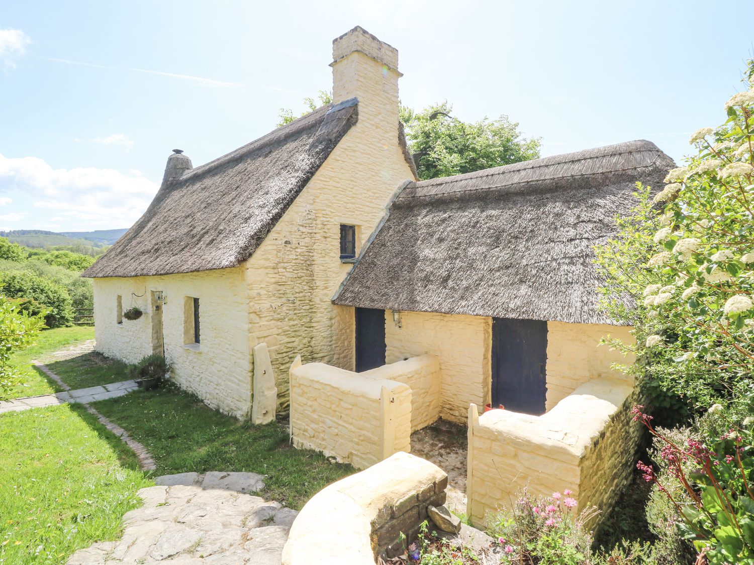 A thatched cottage with yellow stone walls blue doors and a small garden path at Thatched Cottage in Llanybydder