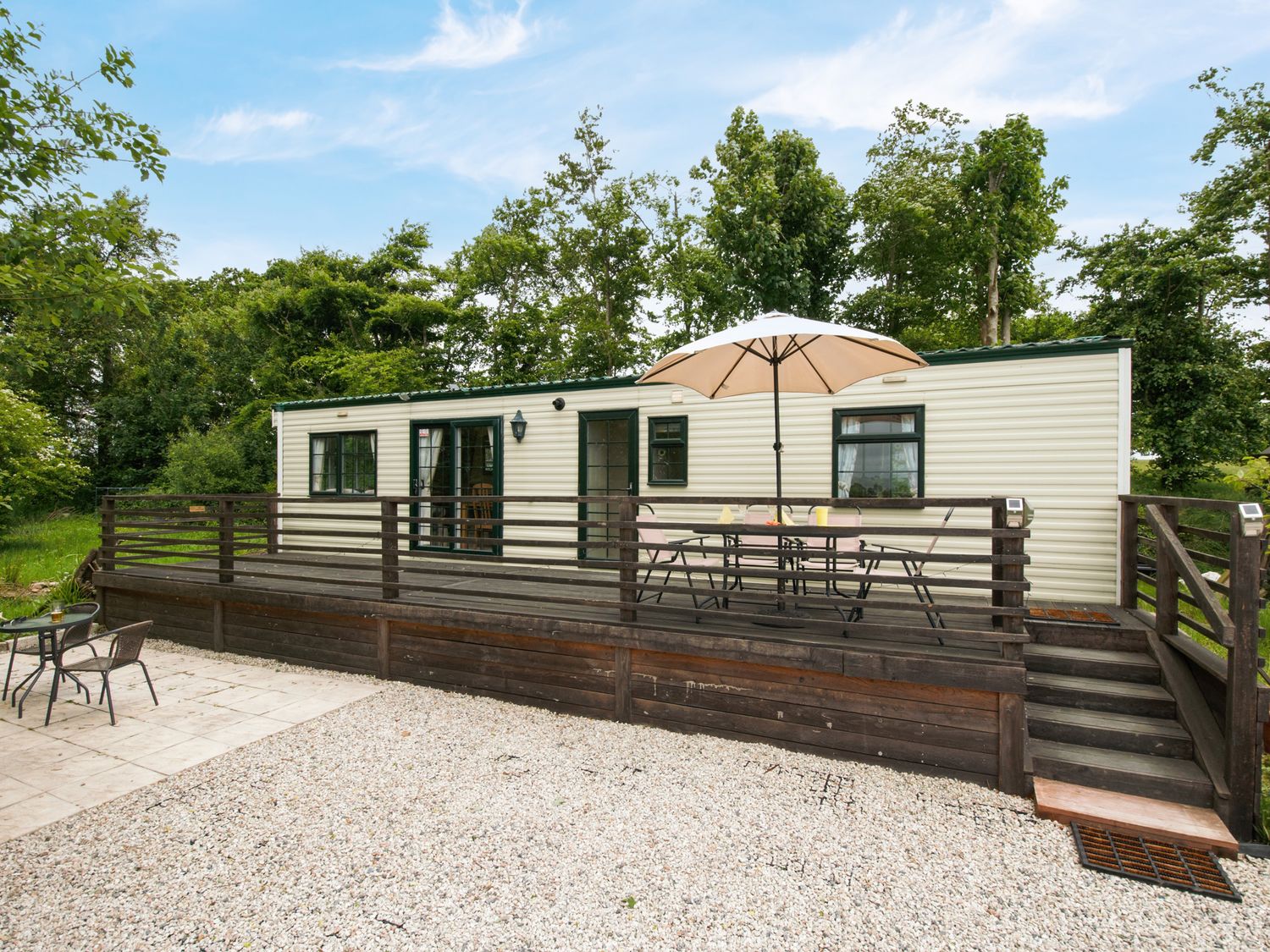 A mobile home with a wooden deck table and chairs with umbrella in front at Little Malory in St Giles-On-The-Heath
