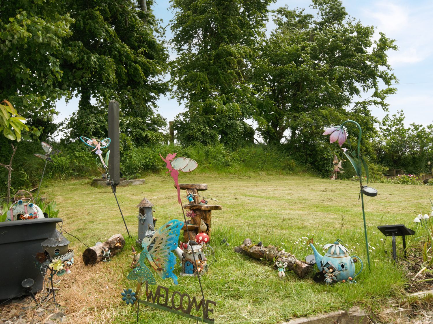 A garden area with fairy-themed decorations a log and trees at Little Malory in St Giles-On-The-Heath
