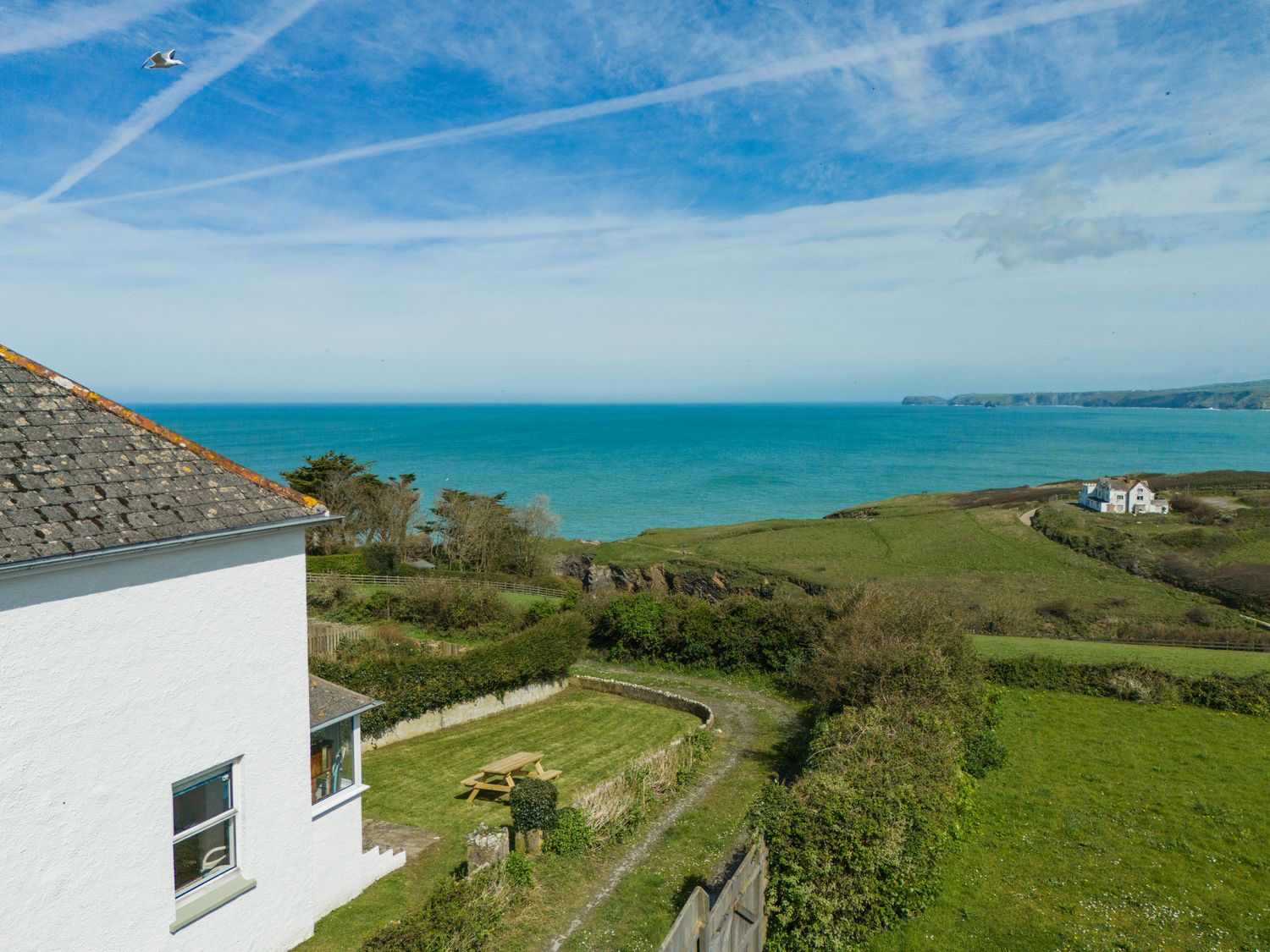 A white house overlooking the ocean with greenery and a picnic table at Tamarama House in Port Isaac