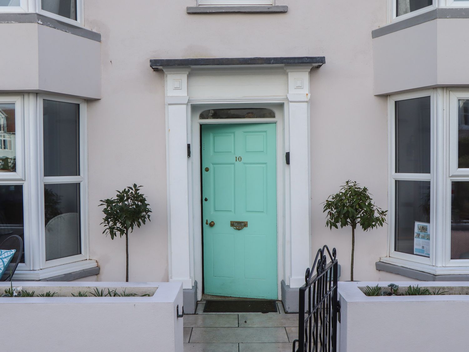 A front door painted turquoise flanked by two small trees in planter boxes at Sanctuary Cottage in Shaldon