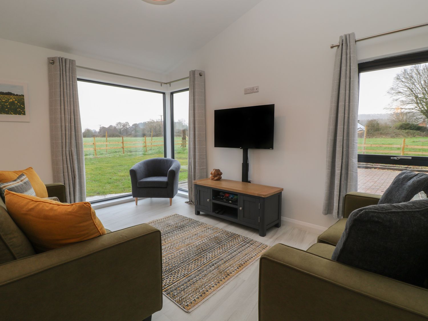 A seating area with two armchairs a TV on a stand and large windows showing an outdoor view at The Cook House in Erlestoke near Great Cheverell
