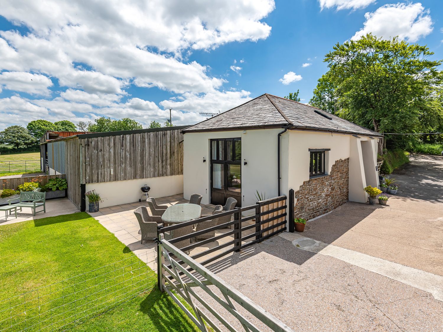 A small building with a patio dining set outside and a wooden fence with a gate at Waterland Old Barn in Bradworthy