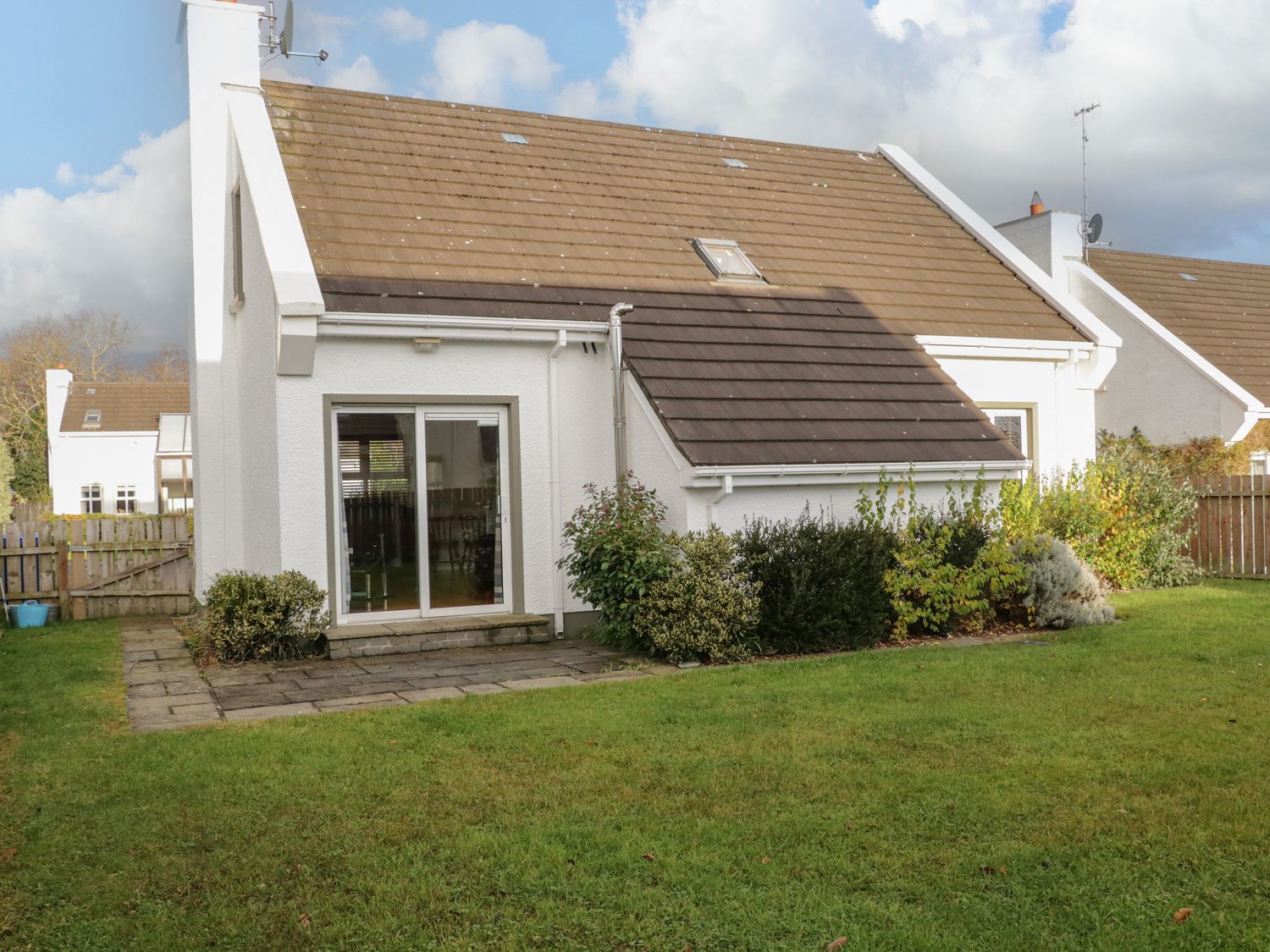 A white house with a brown roof and garden with green grass and shrubs at Sea Spray Cottage in Rathmullan County Donegal