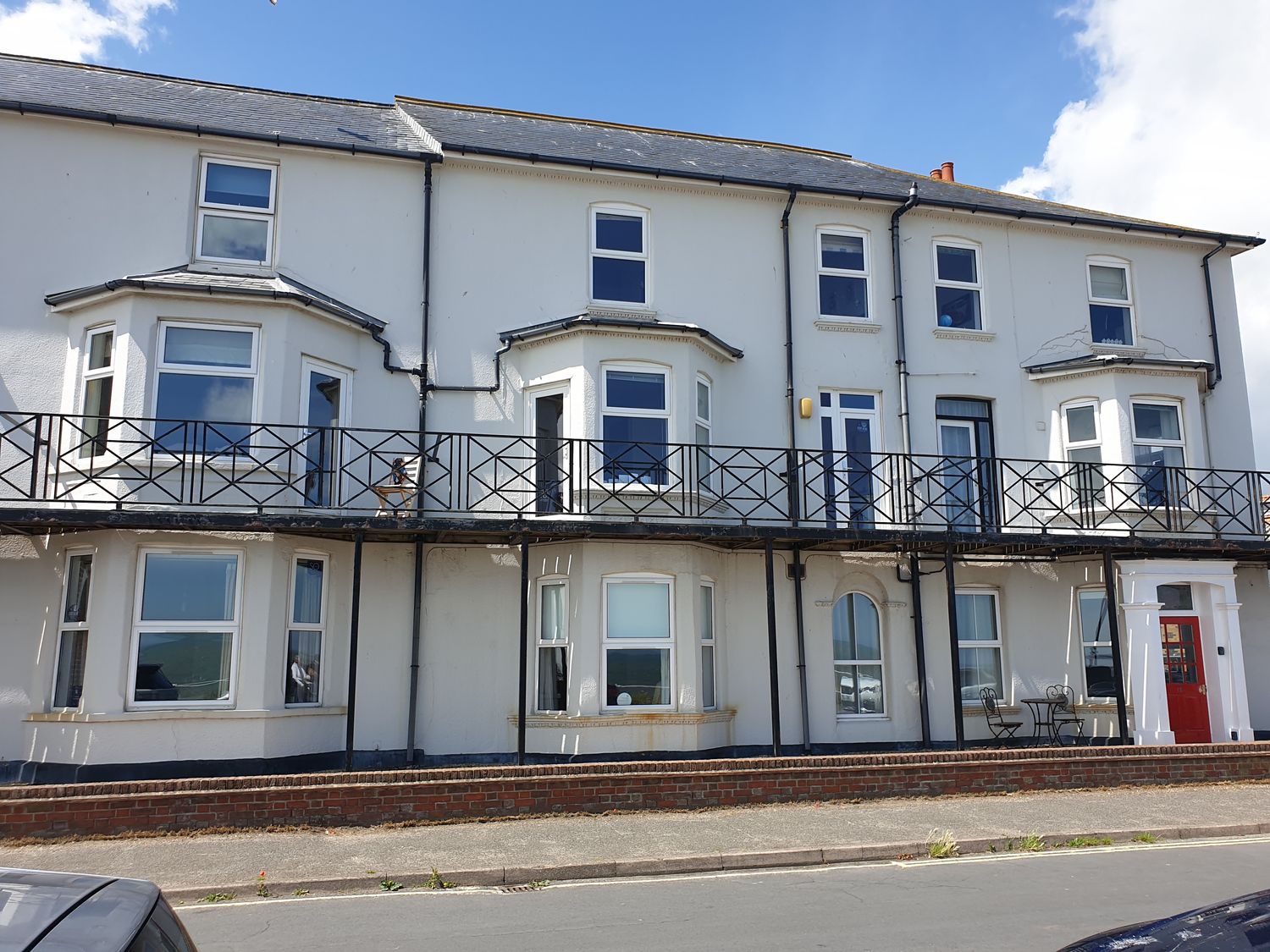 A two-story white building with multiple windows and balconies and a red door at 11 The Craighurst in Southwold