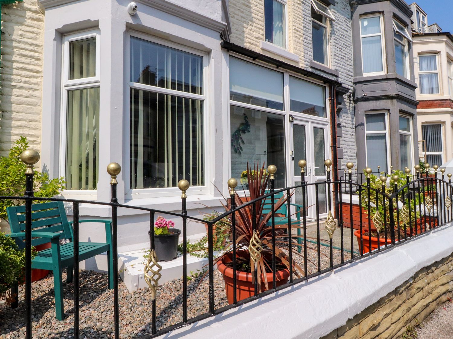 The front exterior of a terraced house with large windows metal fence green chairs and potted plants at Verdo House in Blackpool