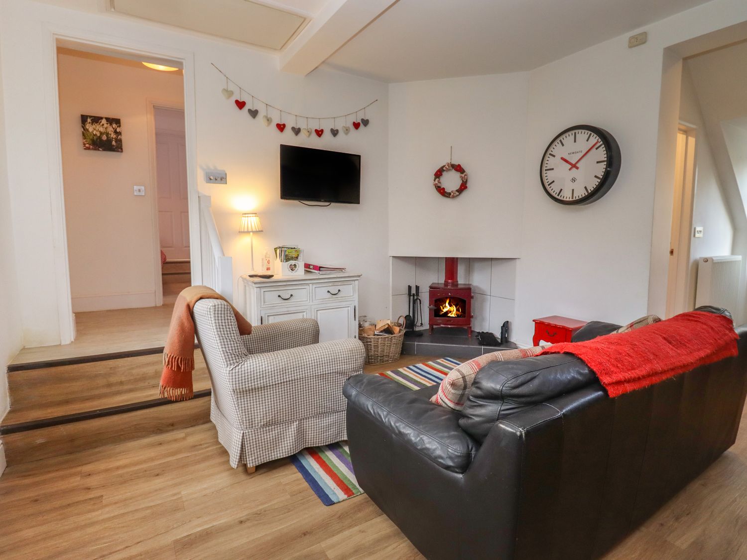 A living room with a leather sofa a checkered armchair a fireplace and a wall clock at The Little White Cottage in Milton-Under-Wychwood