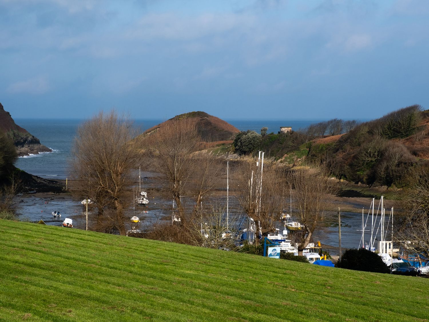 A coastal landscape with boats docked near shore and grassy hill in foreground at Watermouth Castle Bassett Apartment Berrynarbor near Ilfracombe