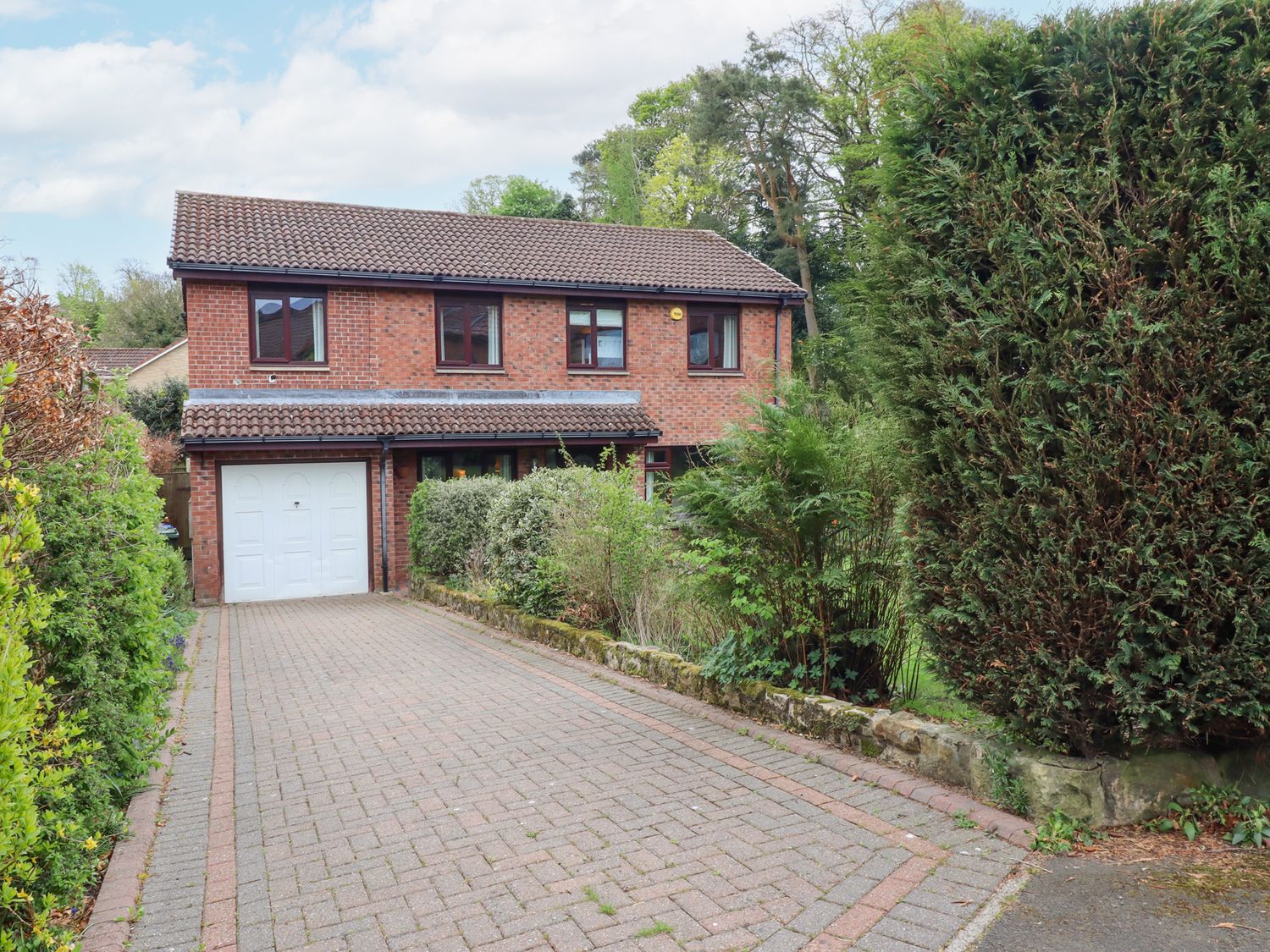 A two-story brick house with a tiled roof garage and a paved driveway surrounded by bushes at Sparrow House in Alnwick