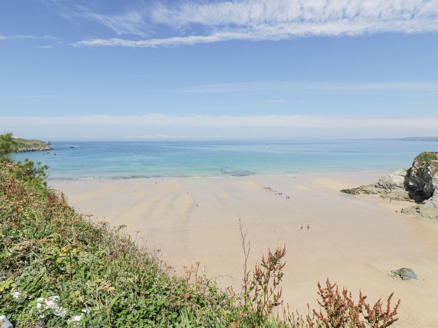 A sandy beach with people near the shoreline and vegetation in the foreground at 17 Ocean Heights in Newquay